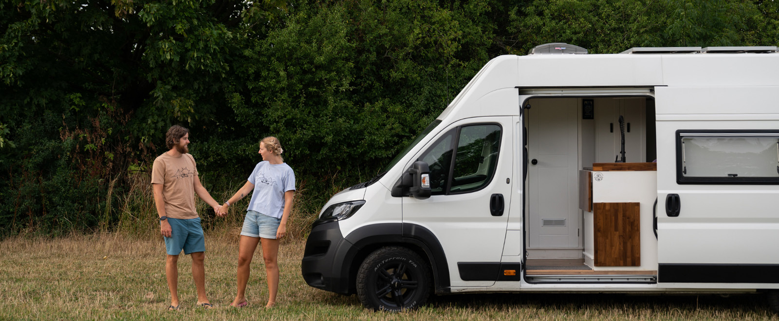 Jess and Marcus holding hands next to their campervan